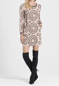 Vestido beige de manga larga con patrones circulares negros, presenta bolsillos laterales. Combinado con botas de tela negras hasta el muslo.
