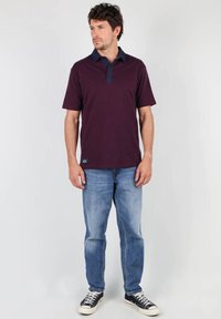 Polo bordeaux avec un col marine, à manches courtes et un logo sur le côté. Assorti à un jean bleu clair et des baskets noires. Design simple et décontracté.