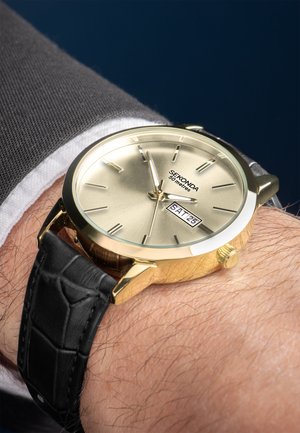 Gold wristwatch with a round face, black leather strap featuring crocodile pattern, and a date display showing SAT 25.