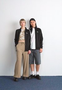 Sorte atletisk jakker med hvide detaljer, beige ribbede bukser og denimshorts. Uformelt fodtøj, neutrale farver, minimalistisk design.