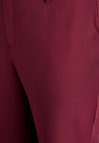 Maroon pants made of smooth fabric, featuring a straight cut with side pockets and a slightly elastic waistband. No visible patterns or accents.