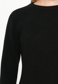 Suéter negro de punto con escote redondo, mangas largas y un tejido suave y texturizado. Sin patrones ni adornos visibles.