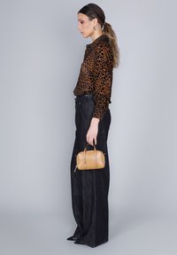 Blusa in stampa leopardata, pantaloni a gamba larga in denim scuro e una piccola borsa a tracolla in pelle beige. La blusa presenta un design con bottoni e una leggera lucentezza.