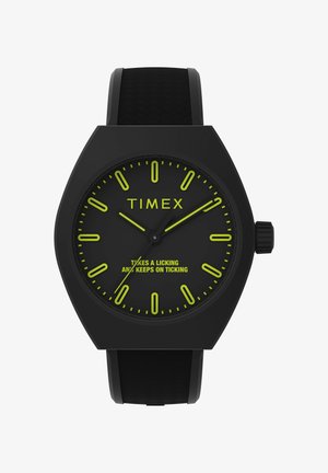 Černé hodinky Timex s hexagonálním pouzdrem, černým silikonovým páskem, svítícími zelenými hodinovými značkami a textem na ciferníku: "Zvládne to a stále tiká."