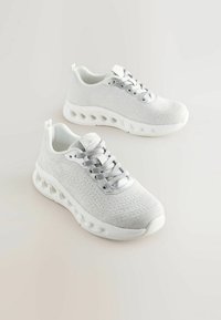 Des chaussures de sport blanches avec un dessus en tricot texturé, un design à lacets et une semelle rembourrée avec des découpes pour un soutien et une ventilation supplémentaires.