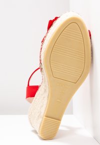 Espadrille roja con suela de yute y fondo de goma texturizada. Presenta un diseño de tira y está marcada con "37" en la suela, fabricada en España.