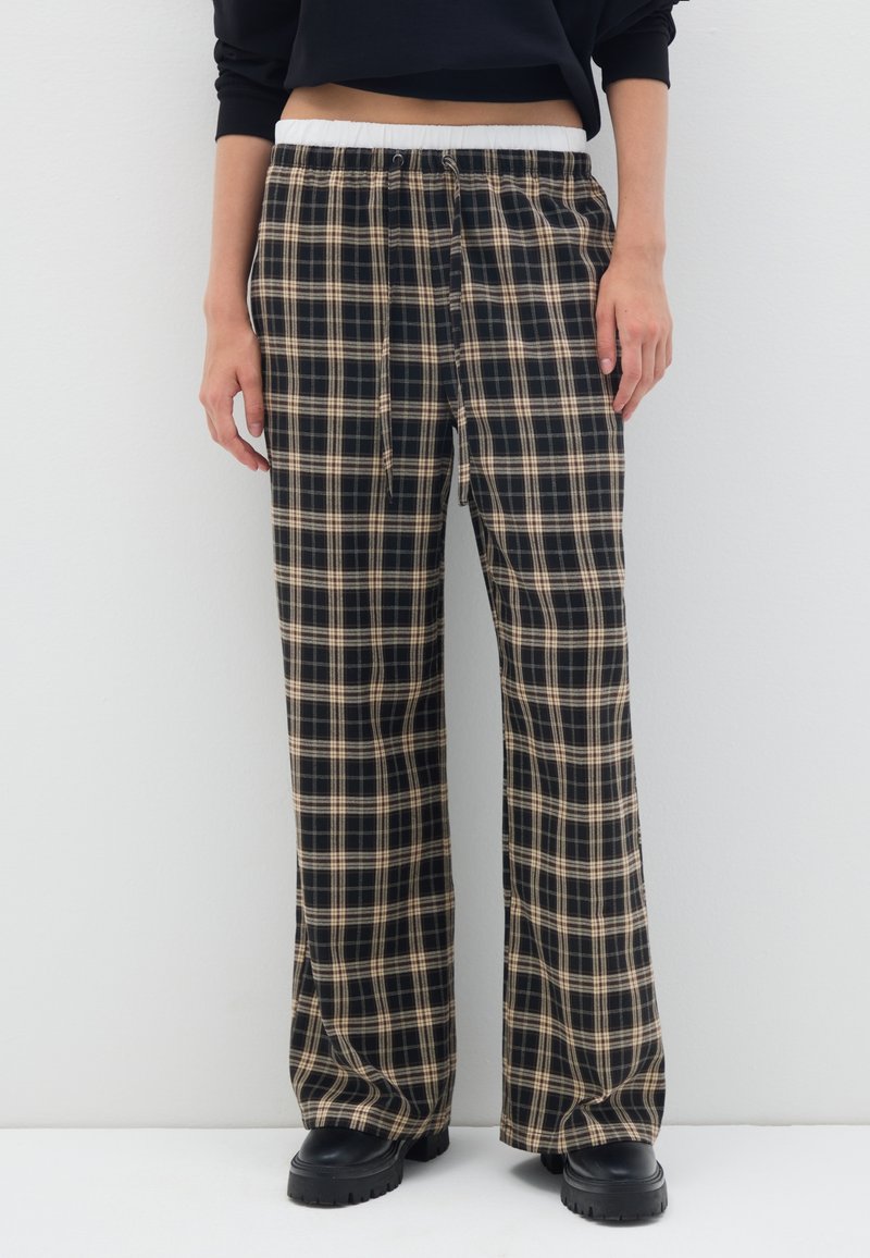 Pantalons de pyjama à carreaux noirs et beiges avec une taille élastique et un cordon de serrage, présentant une coupe évasée et une texture de tissu douce.