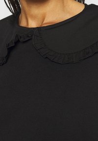 Top nero con colletto rotondo dai bordi arruffati, realizzato in un materiale morbido e liscia. Il design è semplice e minimalista.