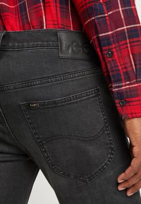 Jeans in denim neri con un'etichetta in pelle sulla cintura, caratterizzati da un design standard della tasca posteriore e dettagli di cucitura laterale.