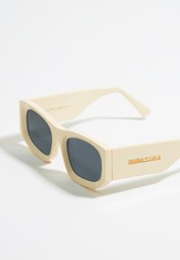 Gafas de sol de montura cuadrada con aros de plástico color crema y lentes oscuros. Presentan la marca "BIMBA Y LOLA" en color naranja en el costado.