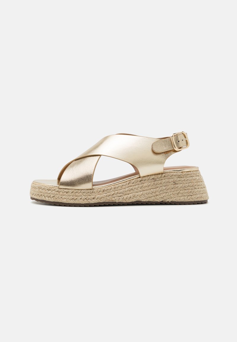 Metallic gold espadrille sandals with cross straps, woven jute wedge sole, adjustable buckle, and smooth upper surface texture.