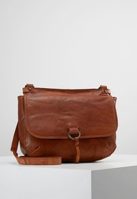 Brun læder crossover taske med klaplukning, metalring detalje, justerbar strop og blød tekstur. Kompakt design med minimalistiske funktioner.