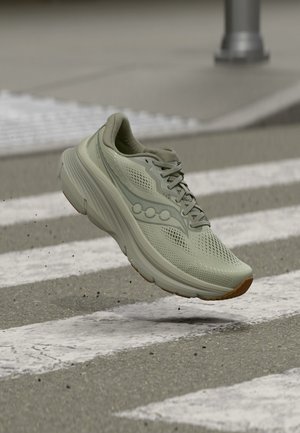 Ανοιχτό πράσινο αθλητικό παπούτσι στον αέρα πάνω από διάβαση πεζών σε πλακόστρωτο δρόμο, με μικρά σωματίδια χαλικιού διασκορπισμένα από κάτω.