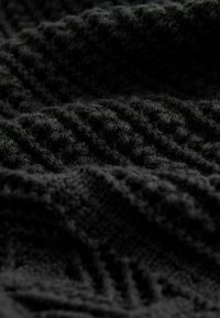 Tissu tricoté noir avec des textures variées, présentant des motifs en relief et une surface douce et pelucheuse. Le matériau semble épais et confortable.