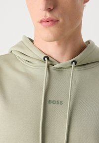 Sudadera verde claro hecha de una tela suave, con capucha ajustable y un pequeño logo "BOSS" en color coincidente en la parte delantera.
