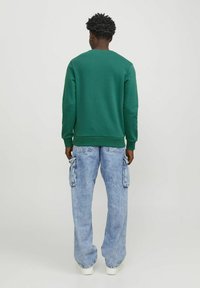 Groene sweatshirt met lange mouwen, geribbelde manchetten en halslijn, gecombineerd met lichtblauwe cargobroek met zijzakken en een relaxte pasvorm.