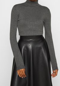 Maglione grigio a collo alto con maniche lunghe, realizzato in un tessuto a maglia texturizzata, abbinato a una gonna in pelle nera a vita alta.