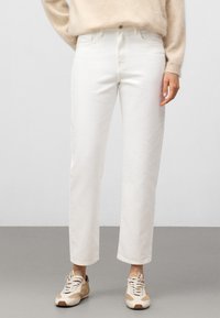Białe dżinsy o prostym kroju z podwiniętym dołem, wykonane z denimu. Połączone z beżowymi trampkami i lekkim, przytulnym swetrem.
