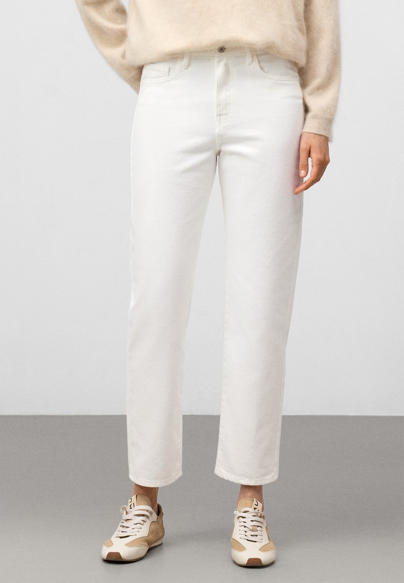 Białe dżinsy o prostym kroju z podwiniętym dołem, wykonane z denimu. Połączone z beżowymi trampkami i lekkim, przytulnym swetrem.