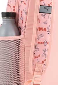 Zaino in tessuto rosa con una tasca laterale in rete che contiene una borraccia grigia, caratterizzato da un motivo di animali giocosi e un accento con logo.