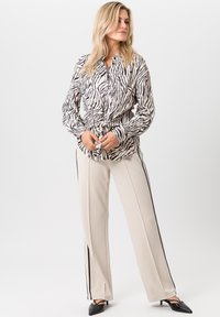 Blouse à motifs zébrés en noir et blanc, assortie à un pantalon large crème avec des bandes noires sur les côtés et des talons aiguilles noirs.