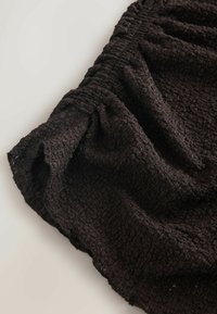 Black textured fabric with a crinkled design, featuring a gathered elastic waistband and flowing drape. Focus on the intricate weave detail.