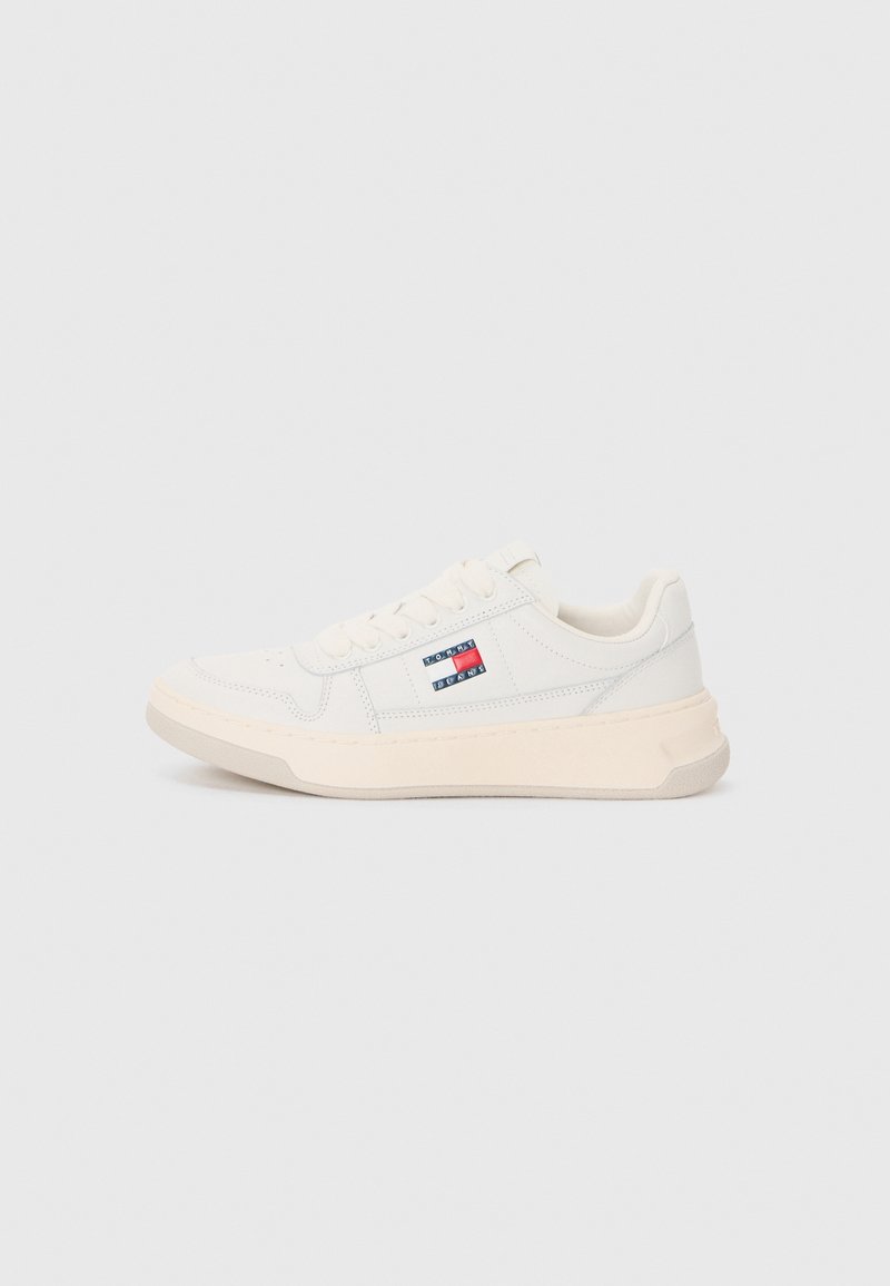 Baskets basses blanches avec semelle beige clair, fermeture à lacets à l'avant, et petit logo rectangulaire rouge, blanc, bleu Tommy Jeans sur le côté.