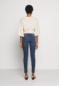 Vaalea harmaa ylisuuri t-paita, jossa on leveät hihat, yhdistettynä tummansinisiin kapeisiin farkkuihin, joissa on takataskut ja sileä farkkutekstuuri.