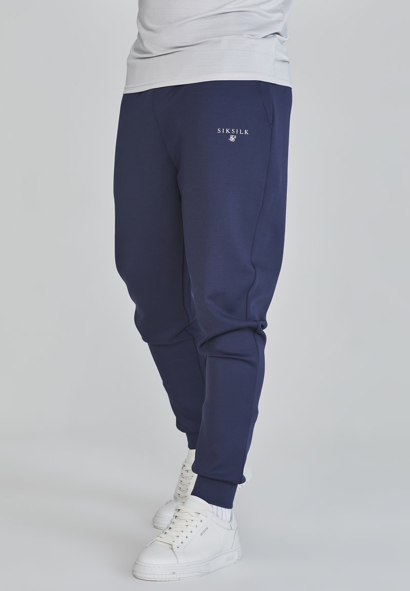 Sötétkék jogging nadrág, which tapered design-nal, elasztikus derékkal és mandzsettákkal rendelkezik. Az anyag sima, bal lábon egy kis logóval.