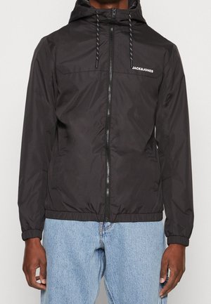 Sort lynlåstrøje med hætte og justerbare snore samt "JACK & JONES"-logo på brystet, båret med lyseblå jeans.