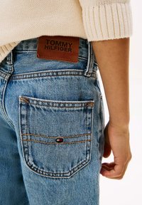 Jeans in denim blu chiaro con un patch in pelle con il logo "TOMMY HILFIGER", dettagli di cucitura visibili e un piccolo logo in accent sulla tasca.