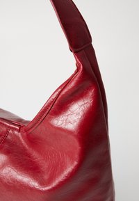 Rote Lederschultertasche mit glatter, glänzender Textur, die eine geschwungene Form und einen breiten Riemen für angenehmes Tragen aufweist.
