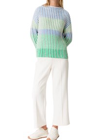 Strickpullover in Blau, Grün und weißen Streifen; weite Ärmel; lockere Passform. Kombiniert mit weißen Hosen und hellen Turnschuhen.