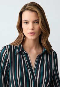 Koszula z długim rękawem w pionowe paski w odcieniach turkusu, czerni i kremu. Z kołnierzykiem, zapinana na guziki, o miękkiej i gładkiej fakturze.