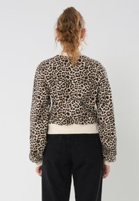 Sweatshirt court à imprimé léopard avec des manches longues et des poignets et un ourlet côtelés. Texture douce, accents crème au niveau du col et de l'ourlet.
