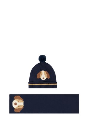 Bonnet en tricot bleu marine avec un motif de visage de chien et un pompon ; écharpe assortie présentant le même motif de chien au centre.