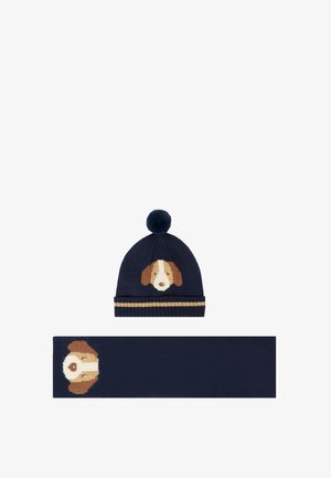 Bonnet en tricot bleu marine avec un motif de visage de chien et un pompon ; écharpe assortie présentant le même motif de chien au centre.