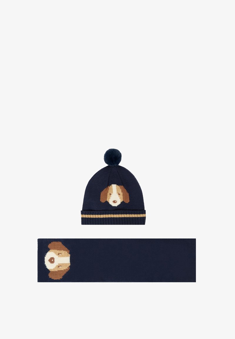 Bonnet en tricot bleu marine avec un motif de visage de chien et un pompon ; écharpe assortie présentant le même motif de chien au centre.