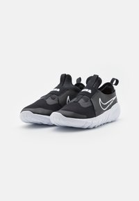 Czarne sportowe buty wsuwane z siateczkowej cholewki, białą podeszwą i akcentami w postaci logo, z zaokrąglonym noskiem i pętelką ułatwiającą zakładanie.