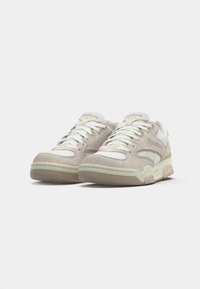Pár béžovo-bielych tenisiek Reebok s detailmi zo suede a siete, bielymi šnúrkami a polstrovanými podošvami na čistom bielom pozadí.