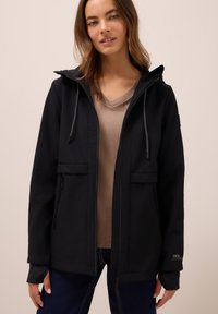 Zwarte softshell jas met ritssluiting aan de voorkant, verstelbare capuchon en twee zakken aan de voorkant. Bevat grijze trekkoorden en details op de manchetten. Minimalistisch design.
