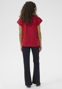 Červené tričko s krátkým rukávem vyrobené z lehkého materiálu, kombinované s tmavě modrými zvonovými džíny. Džíny mají minimální prošití a úzký střih.