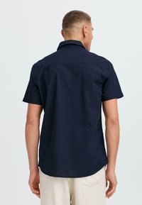 Camisa de manga corta en color navy, confeccionada en una tela texturizada, con un cuello clásico, costura en el yugo trasero y un dobladillo recto.