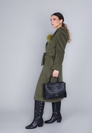 Olijfgroen jas met een gestrikte taille, voorzien van een gestructureerde gele accent; gecombineerd met een zwarte gegraveerde handtas en zwart kniehoog schoeisel.