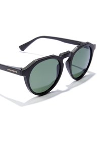Ochelari de soare negri cu ramă octogonală, lentile verzi și branding auriu "Hawkers" pe braț. Textură mată și design elegant.