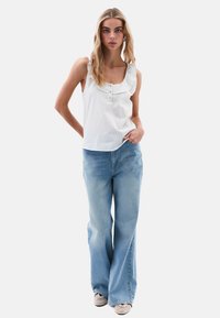 Weißes ärmelloses Oberteil mit Rüschenausschnitt und drei Knöpfen, kombiniert mit hellblauen weiten Jeans. Glatte Stoffqualität und lässige Passform.
