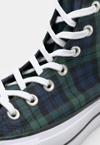 Wysokie sneakersy w kratkę w ciemnozielonym i niebieskim kolorze. Posiadają białe sznurówki i metalowe oczka, czarną gumową podeszwę z białym wykończeniem.