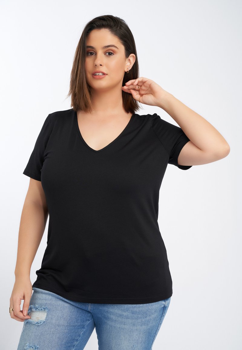 Zwarte V-hals t-shirt van zacht materiaal, met korte mouwen en een ontspannen pasvorm. Gecombineerd met lichtblauwe distressed jeans.