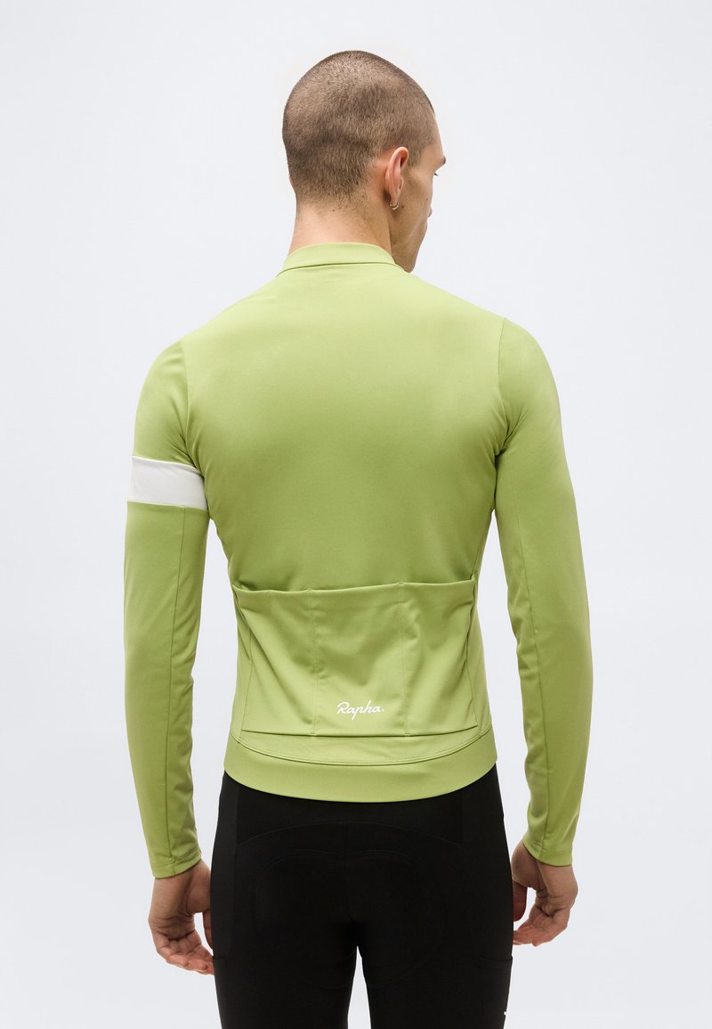 Mann trägt hellgrünes langärmeliges Radtrikot mit Rückentaschen und einem weißen Streifen am linken Arm, von hinten gezeigt.