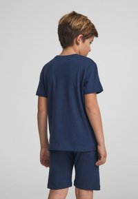 T-shirt in cotone blu navy con maniche corte e collo rotondo, abbinato a pantaloni corti in cotone coordinati. Design semplice e casual senza motivi o accenti.